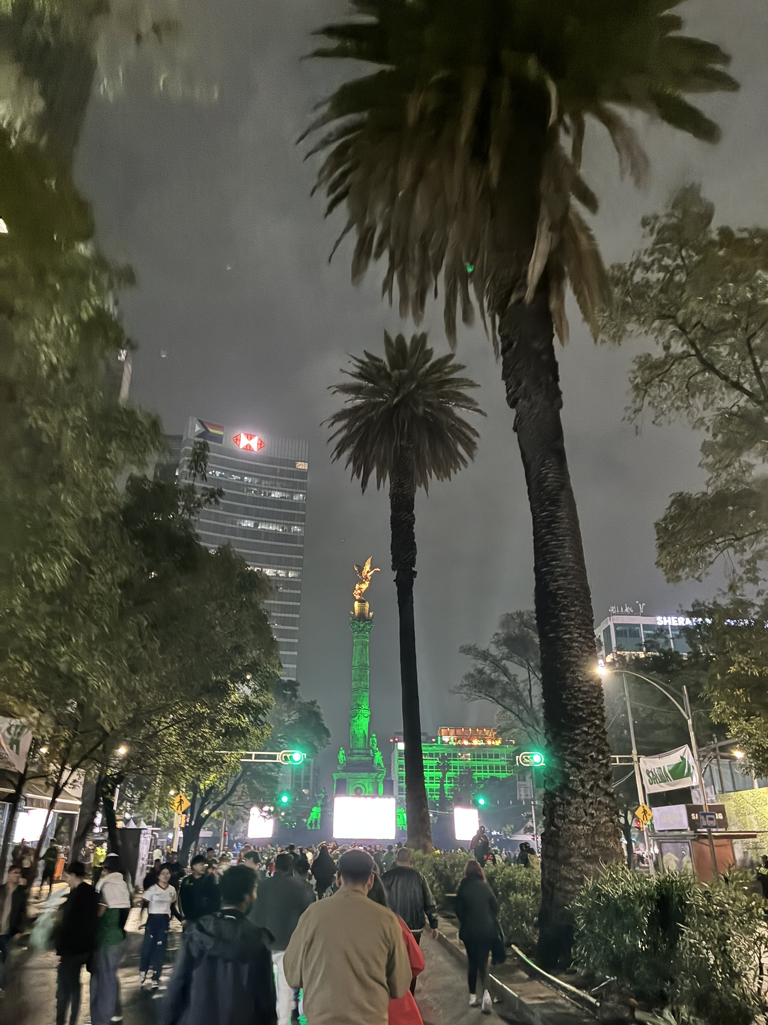 The Angel of Independence monument in Mexico City lit up green at night with a crowd gathered below