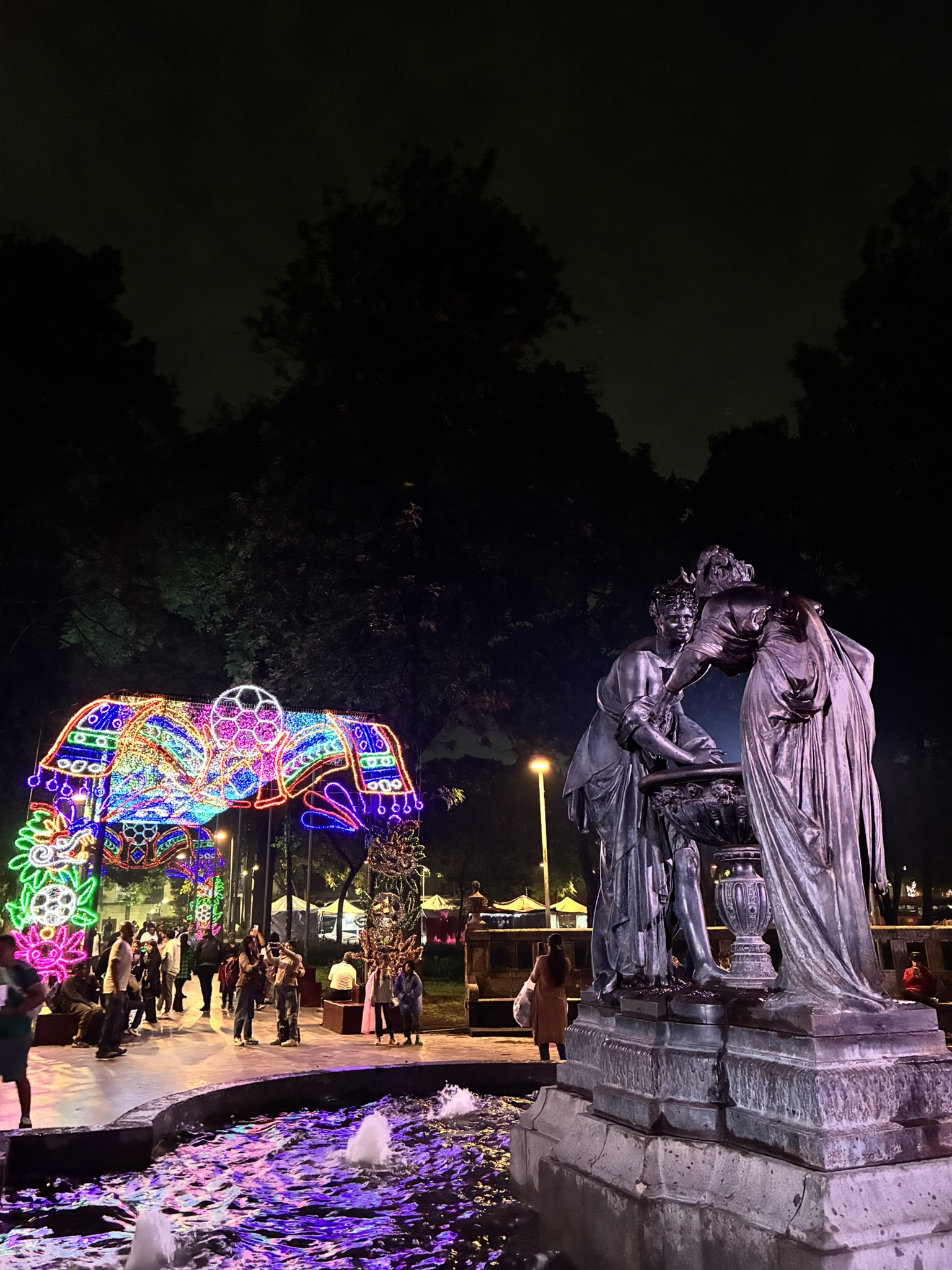 A fountain statue at night surrounded by colorful World Cup light installations