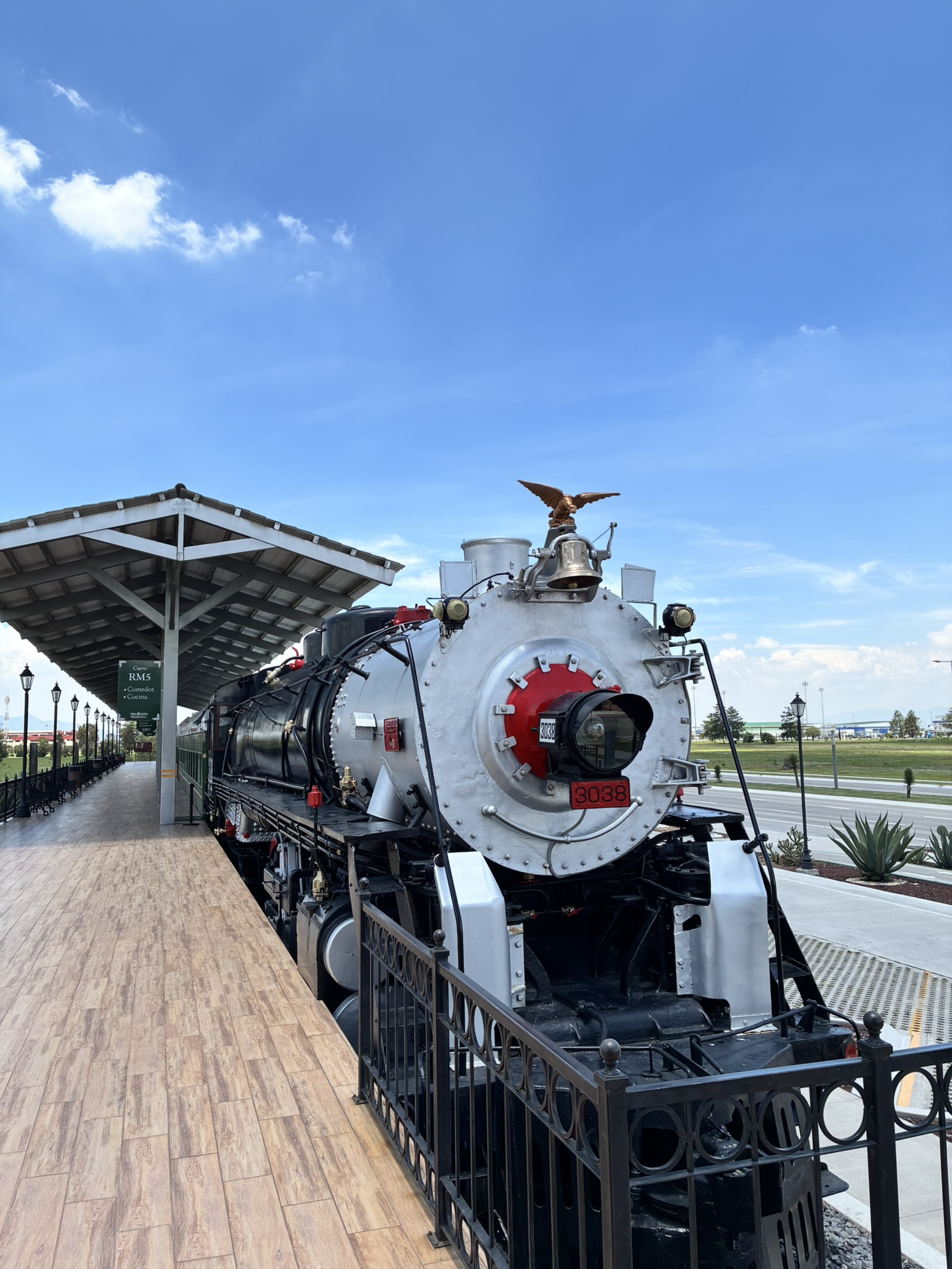 A restored vintage steam locomotive with a golden eagle ornament on the front, on display at a railway museum under a blue sky