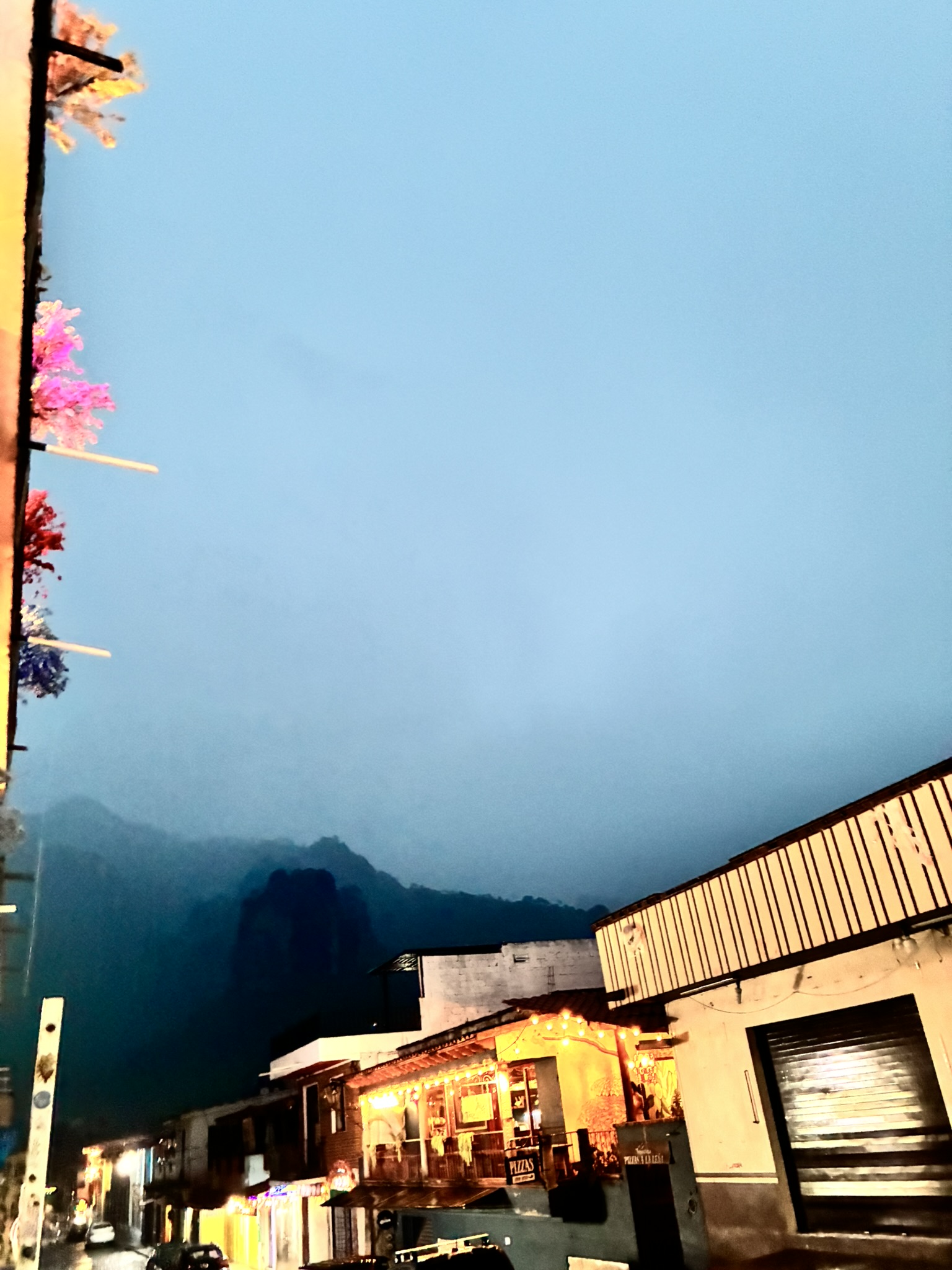 An evening street in Tepoztlán with string lights, a lit restaurant, and mountains in the background