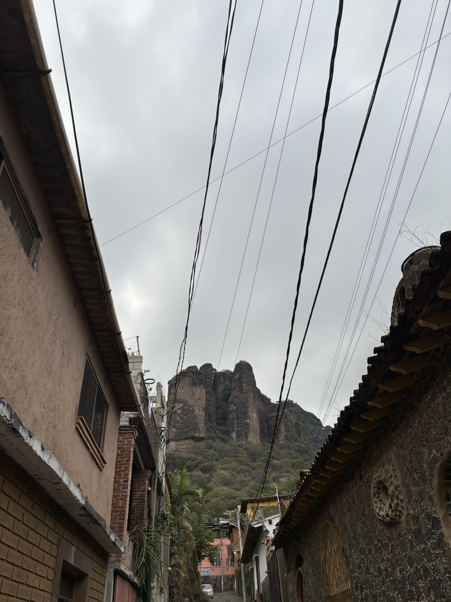 A narrow street between houses in Tepoztlán with the jagged Tepozteco mountain rising above the rooftops