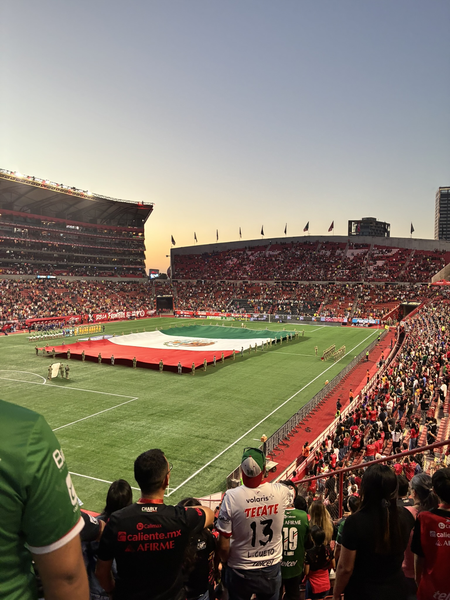A packed stadium with a giant Mexican flag stretched across the field before a match